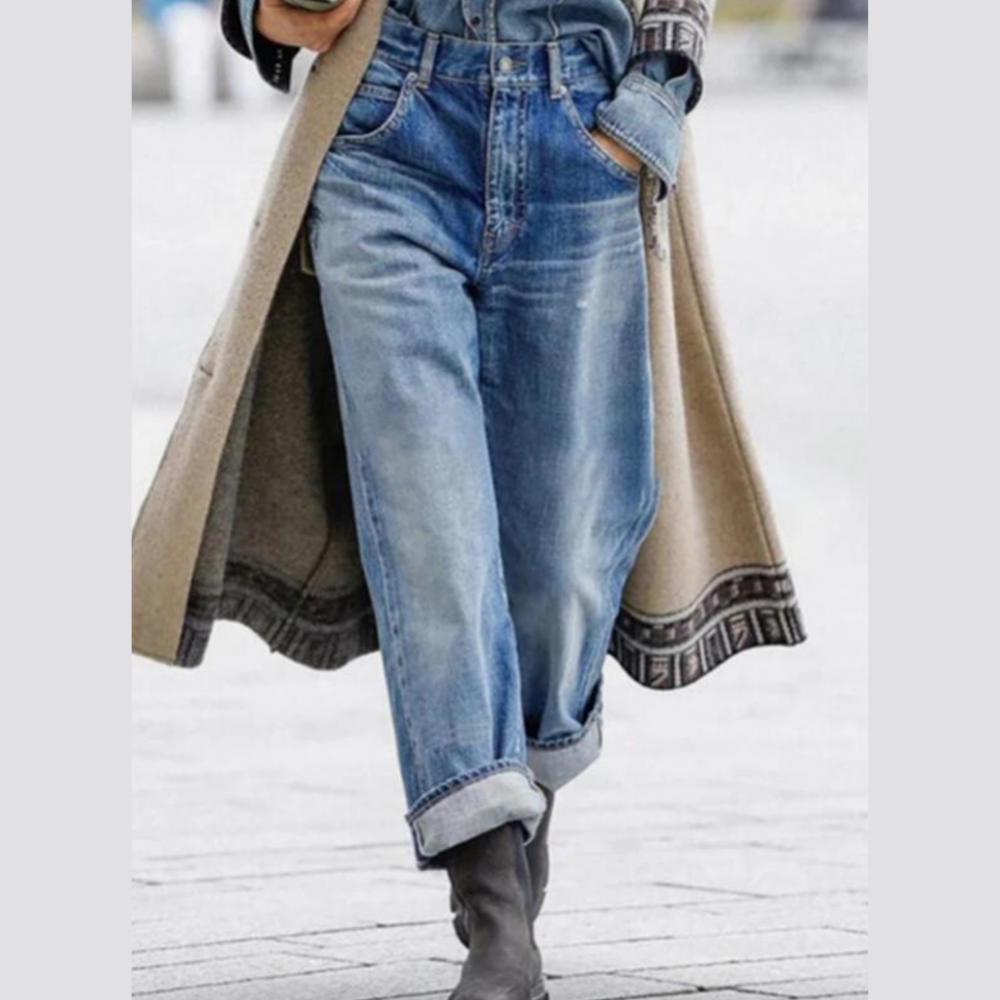 Person in blauer Jeans und Stiefeln, trägt langen Mantel, modischer Streetstyle-Look.