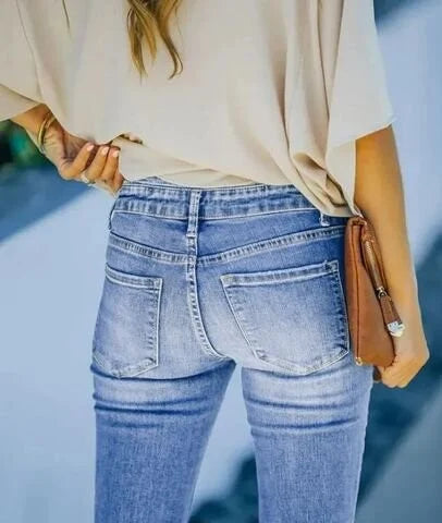 Frau in blauer Jeans und beigem Oberteil, hält braune Clutch, modisch, lässiger Stil.