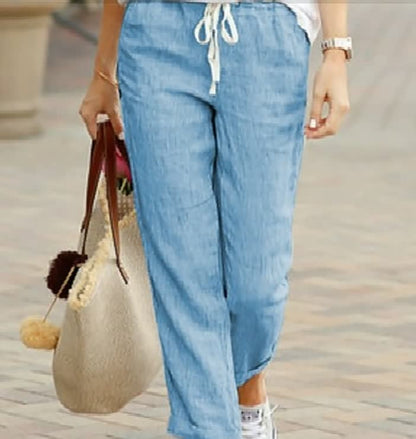 Frau in blauer Leinenhose mit Kordelzug, hält beige Tasche, lässiger Sommerlook.