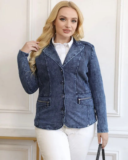 Frau in blauer Jeansjacke, weißer Bluse und weißer Hose vor weißer Wand.
