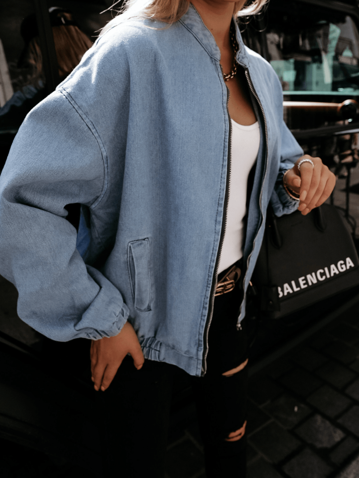 Frau in blauer Jeansjacke, weißem Top, schwarze Tasche, modisch, urbaner Stil.