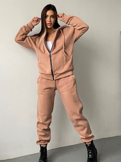 Frau in beigem Jogginganzug, Kapuzenjacke, Jogginghose, schwarze Stiefel, Freizeitmode.