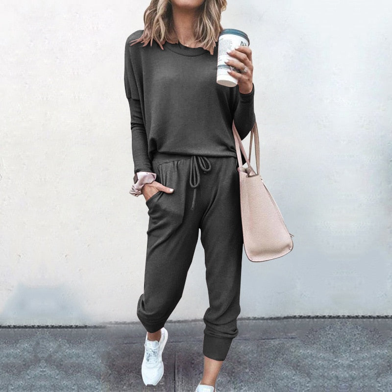 Frau in grauem Jogginganzug mit Kaffeebecher und beiger Tasche, lässige Mode, Straßenstil.