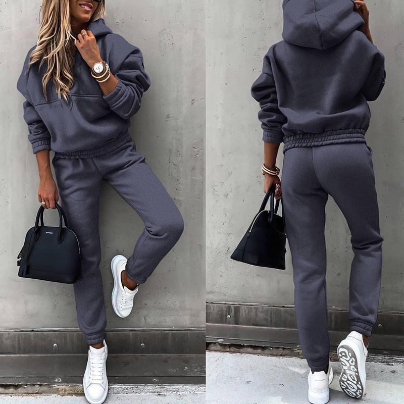 Frau in grauem Jogginganzug, weiße Sneaker, schwarze Handtasche, lässiger Look, Streetwear.