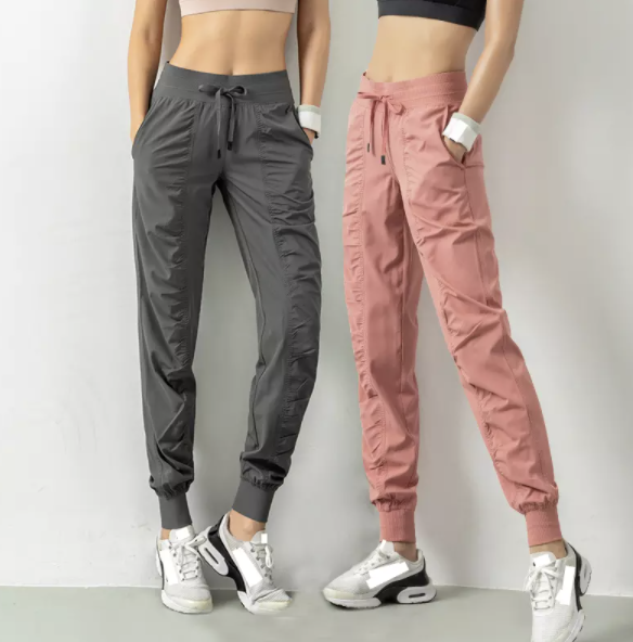 Zwei Frauen in Sportbekleidung, graue und rosa Jogginghose, Sneakers, Fitnessmode.