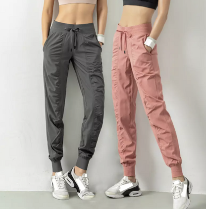 Zwei Frauen in Sportbekleidung, graue und rosa Jogginghose, Sneakers, Fitnessmode.