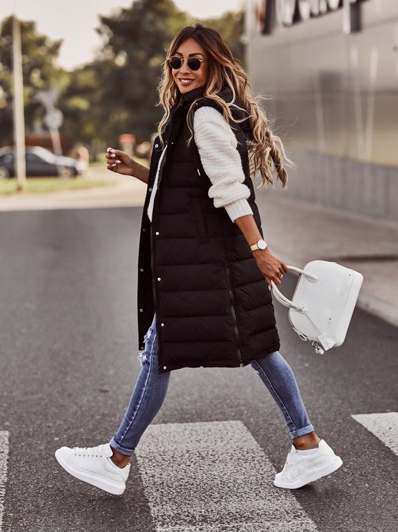 Frau in schwarzer, knielanger Steppweste, weiße Sneakers, Jeans, weiße Tasche, Straße.