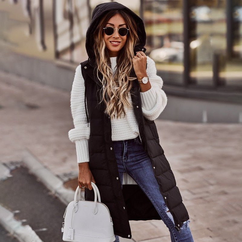 Frau in schwarzer, knielanger Steppweste mit Kapuze, weiße Tasche, lässiger Look.