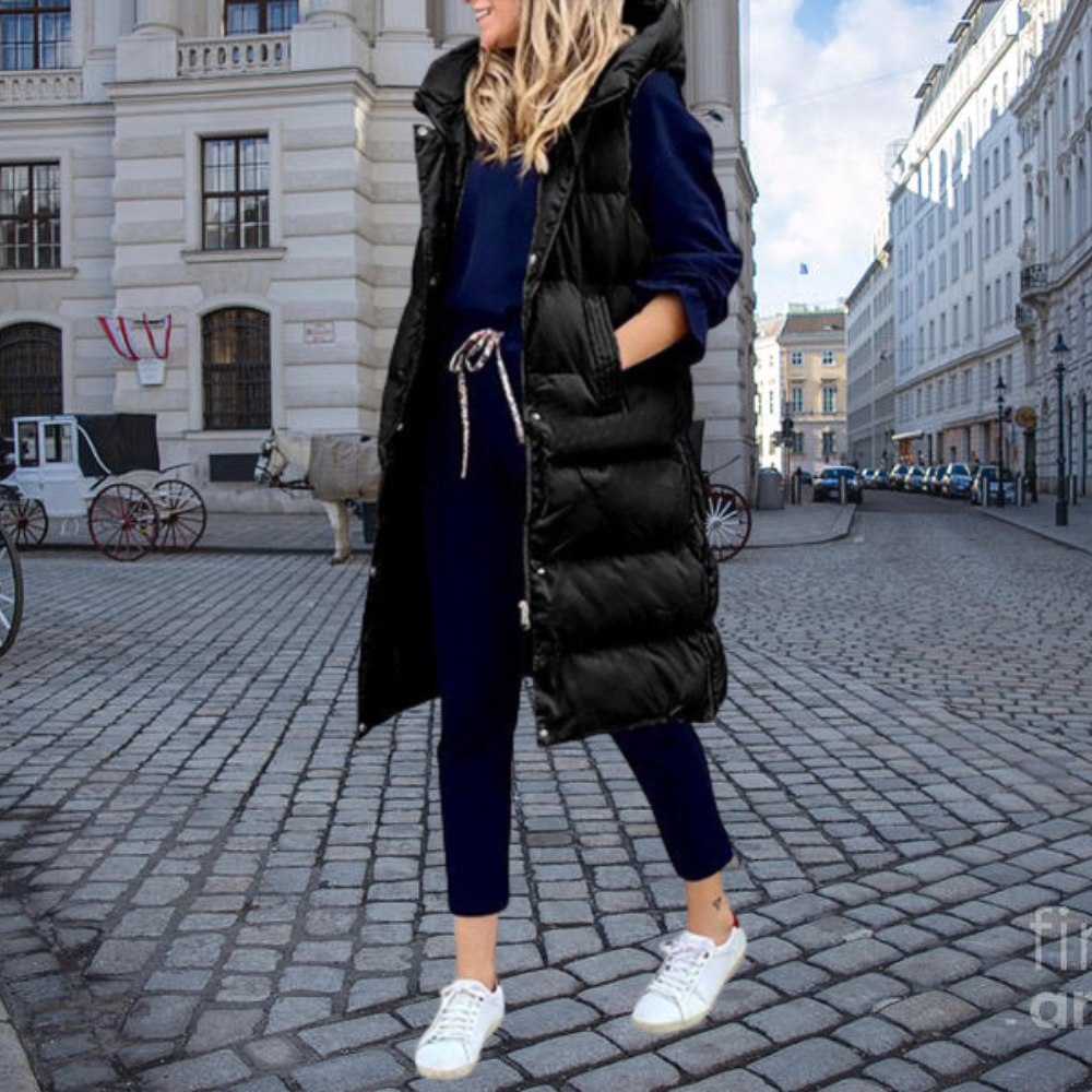 Frau in schwarzer Steppweste, blauer Jogginghose, weißen Sneakers, Stadtstraße im Hintergrund.