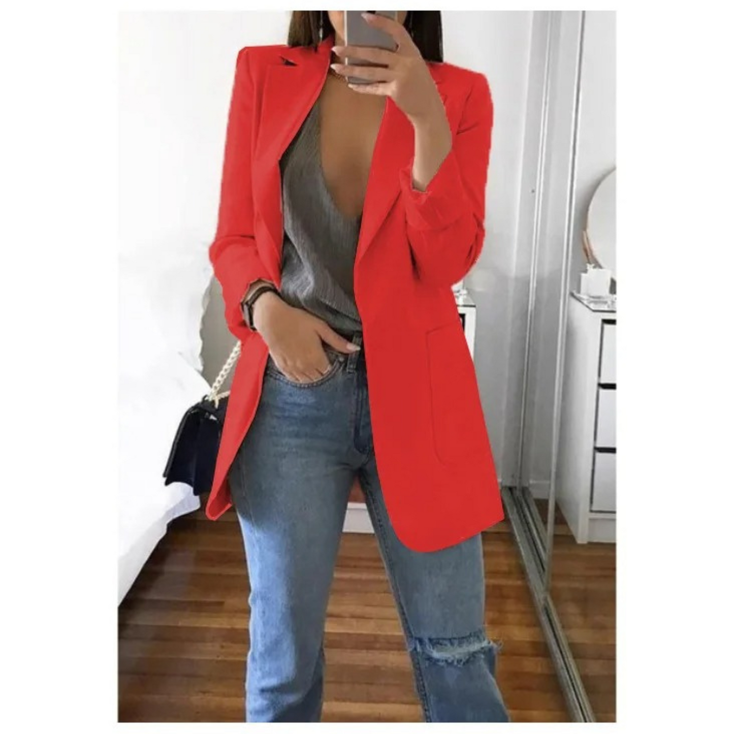 Frau in rotem Damenblazer, grauem Top und blauer Jeans im Schlafzimmer, modisch, elegant.
