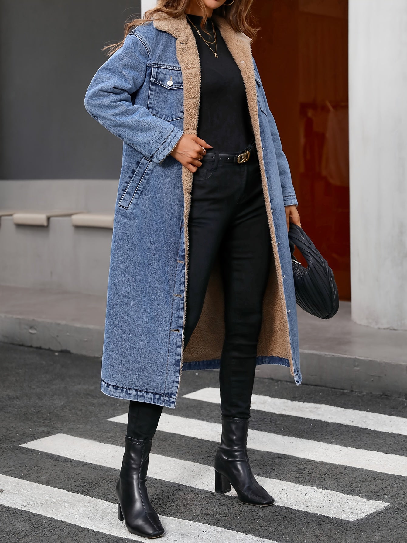 Frau in blauem Jeansmantel mit schwarzem Outfit und Stiefeln auf Zebrastreifen.
