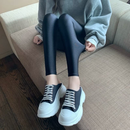 Frau trägt schwarze Leggings und weiße Sneaker auf Sofa, gemütliche Mode, Freizeitkleidung.