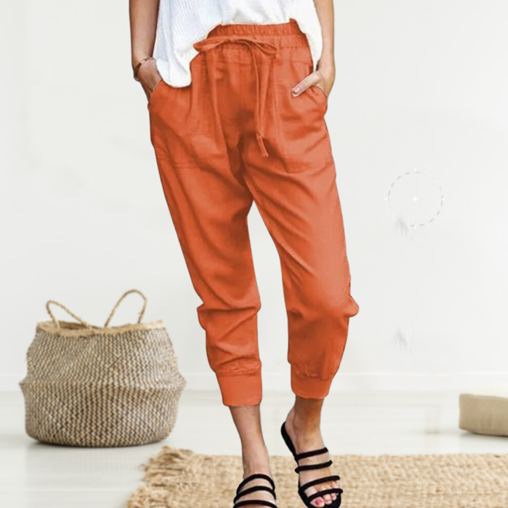 Frau in orangefarbener Leinenhose, lässig, mit Taschen, Sommermode, vor Korb und Teppich.