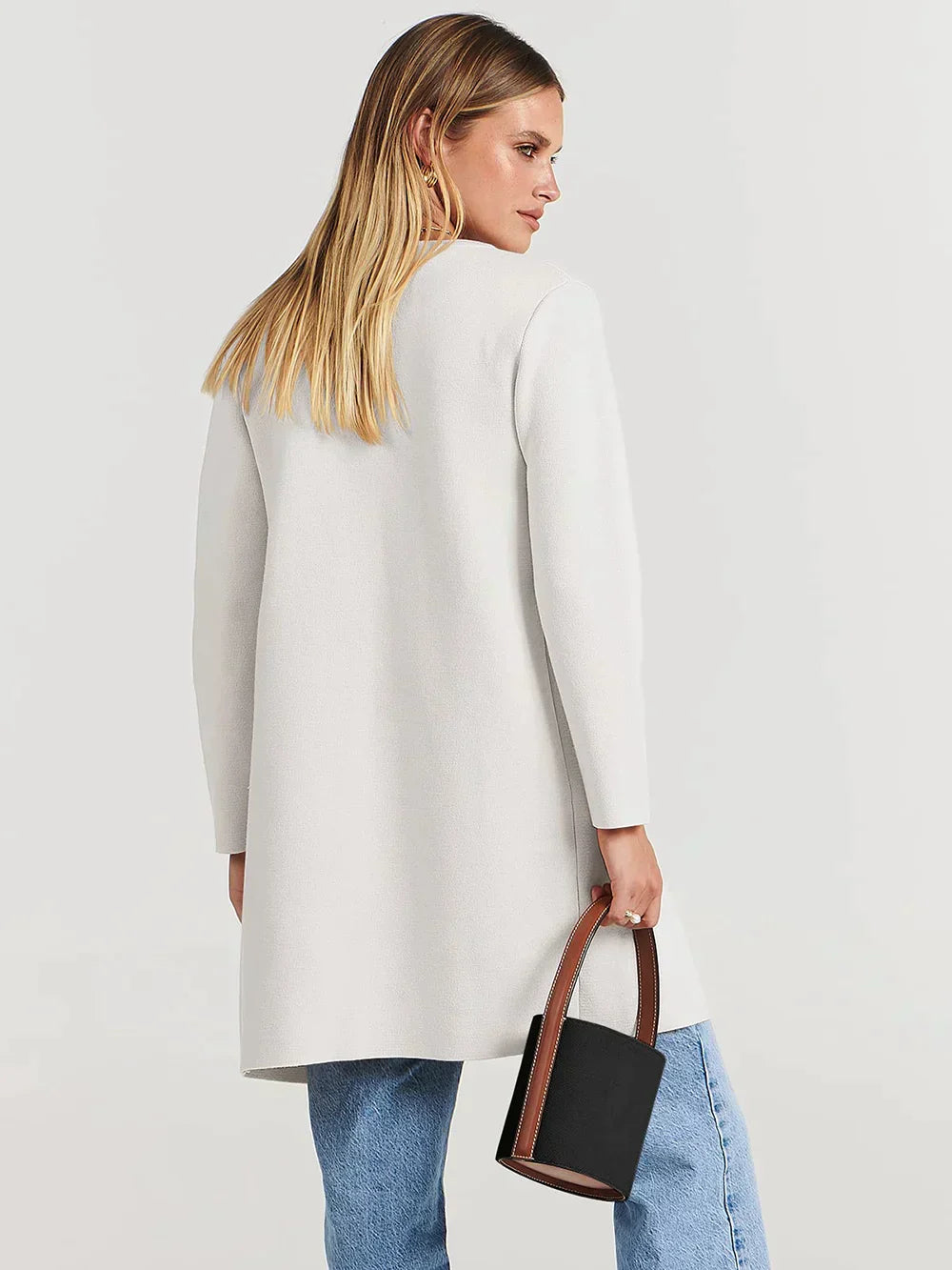 Frau in weißem Mantel, blaue Jeans, schwarze Handtasche, Mode, Damenbekleidung, Rückansicht.