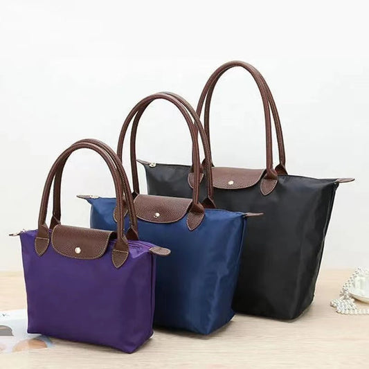 Drei Oxford-Nylon-Handtaschen, wasserdicht, faltbar, in Schwarz, Blau und Lila auf Tisch.