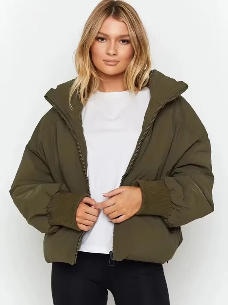 Frau trägt olivgrüne Daunenjacke, weißes T-Shirt, schwarze Hose. Wintermode, Damenbekleidung.