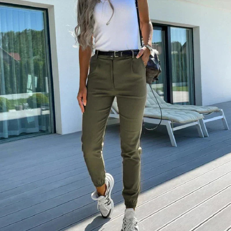 Frau in olivgrüner Hose und weißem Top auf Terrasse, lässiger Stil, Sommermode, Sneakers.