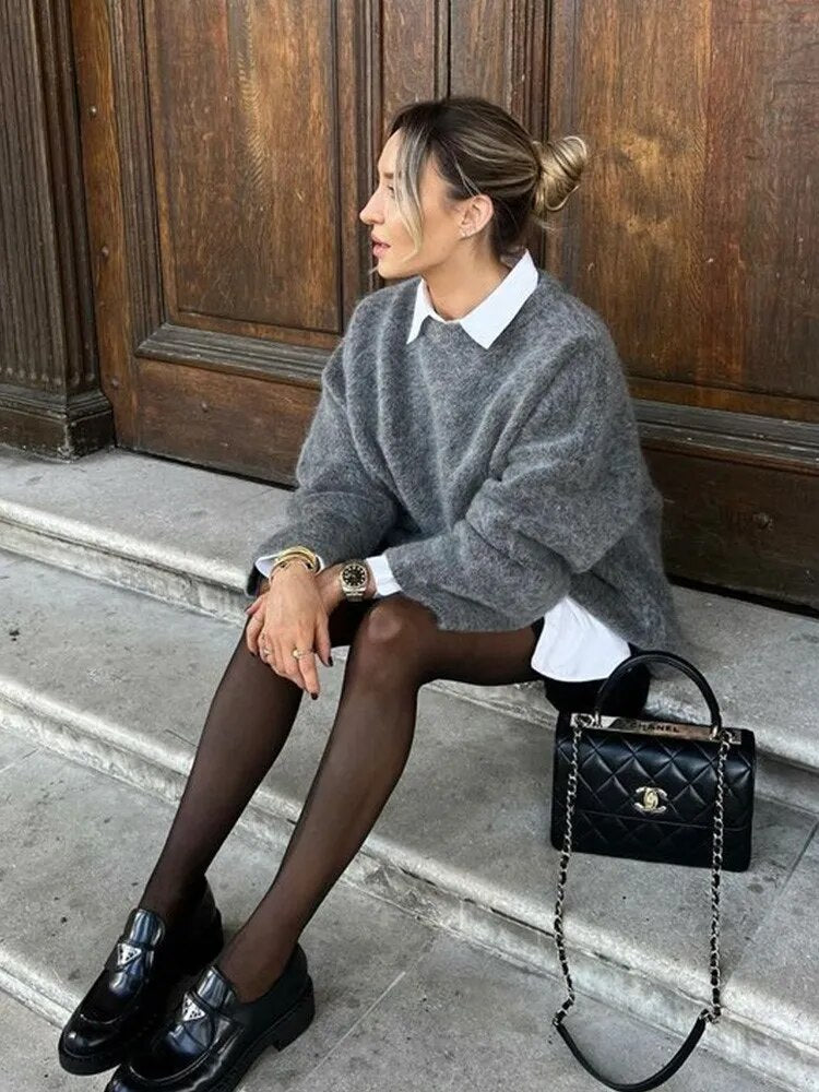Frau in grauem Oversize-Pullover, schwarze Strumpfhose, Ledertasche, Herbstmode 2023.