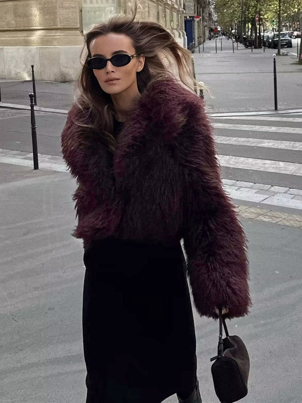 Frau in dunkelrotem Kunstpelzmantel, schwarze Sonnenbrille, Stadtstraße, modisch, elegant.