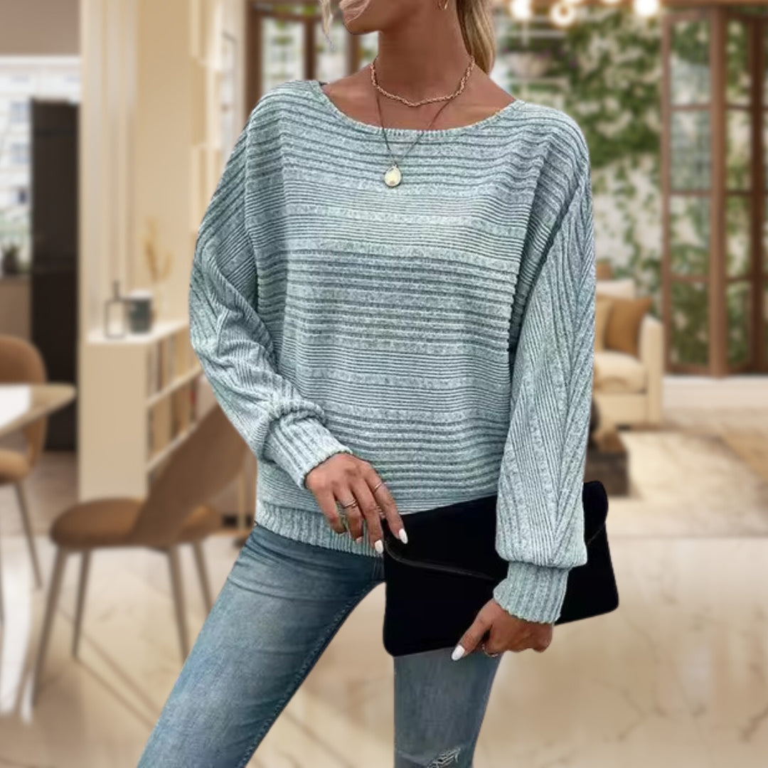 Frau in gestreiftem Pullover, hellblau, Jeans, schwarze Clutch, modernes Wohnzimmer.