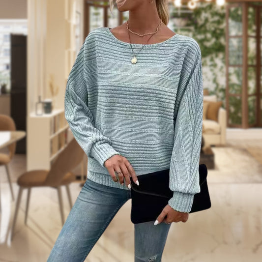 Frau in gestreiftem Pullover, hellblau, Jeans, schwarze Clutch, modernes Wohnzimmer.