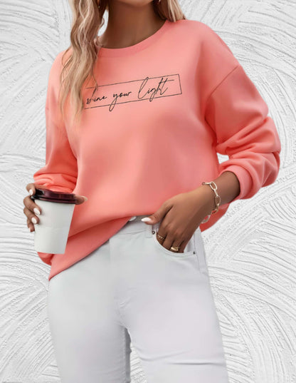 Frau in rosa Pullover mit Schriftzug, hält Kaffeebecher, trägt weiße Hose, modisch, lässig.