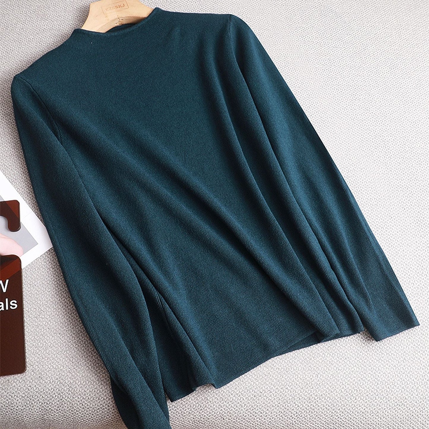 Dunkelgrüner Pullover aus Baumwolle, langärmelig, für Damen, auf grauem Hintergrund.