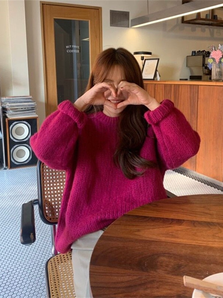 Frau in pinkem Strickpullover formt Herz mit Händen, sitzt in modernem Café.