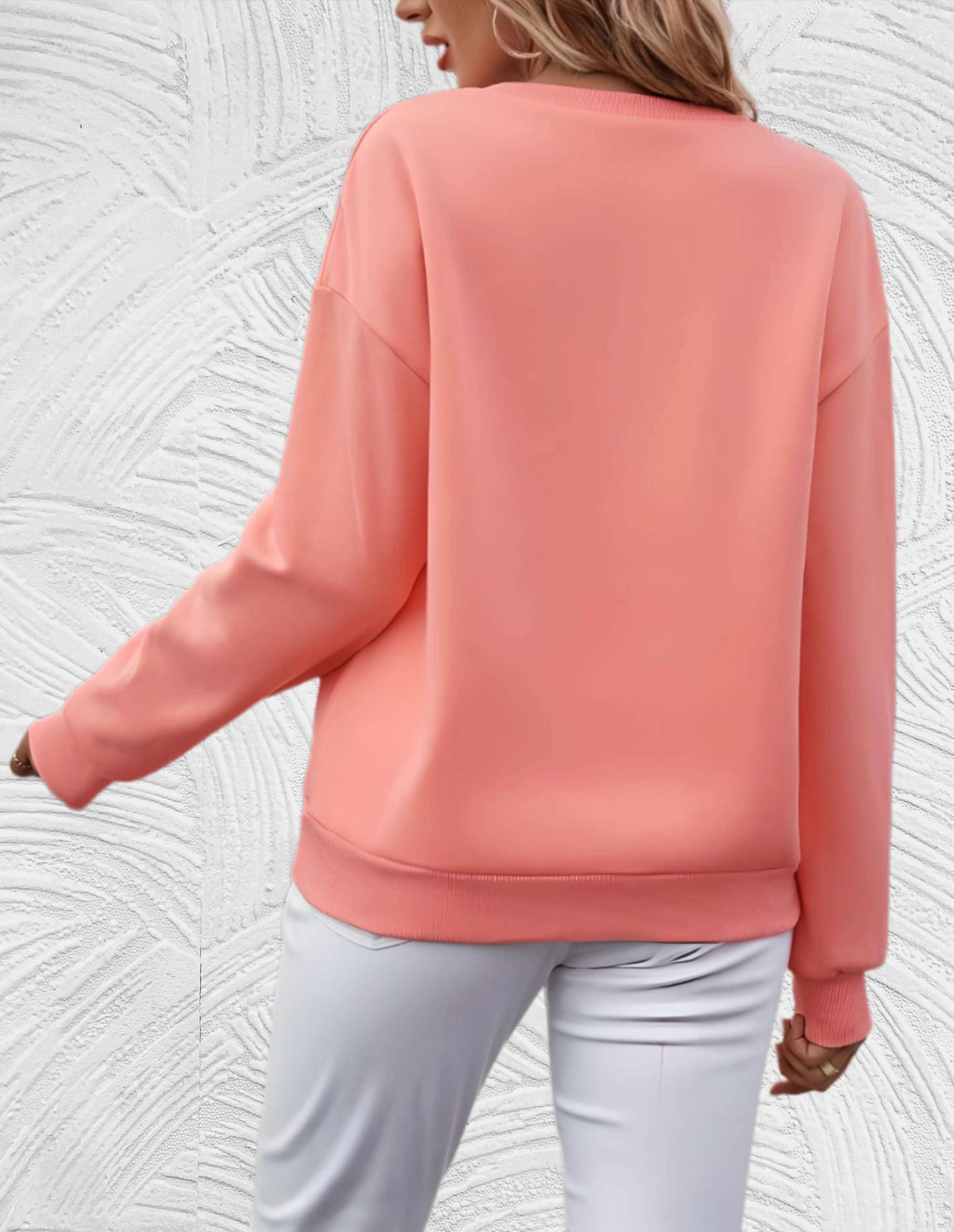 Frau in rosa Pullover und weißer Hose vor strukturiertem Hintergrund, Mode, Damenbekleidung.