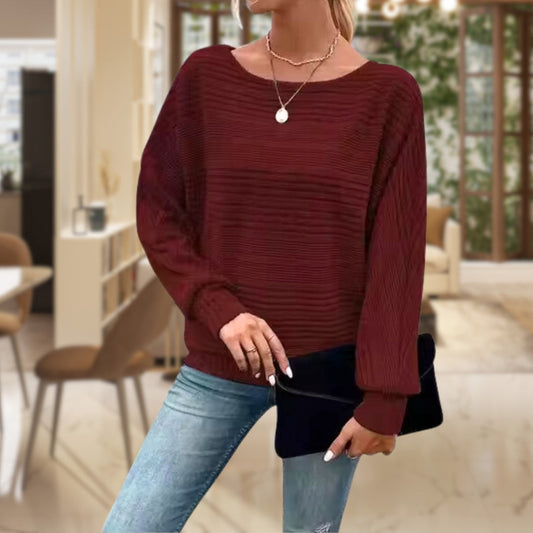 Frau in rotem Strickpullover, blaue Jeans, schwarze Clutch, modernes Wohnzimmer.