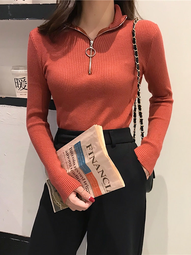 Frau in rotem Strickpullover mit Reißverschluss, hält Zeitung, schwarze Hose, modisch, elegant.