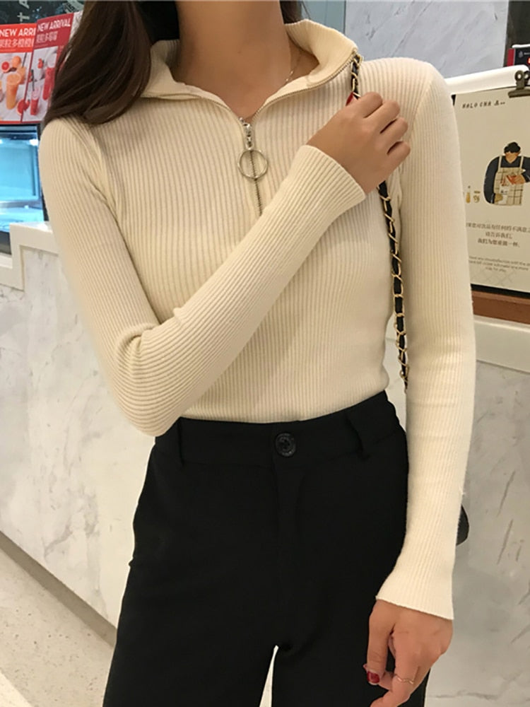 Frau in cremefarbenem, geripptem Pullover mit Reißverschluss, schwarze Hose, modisch, elegant.