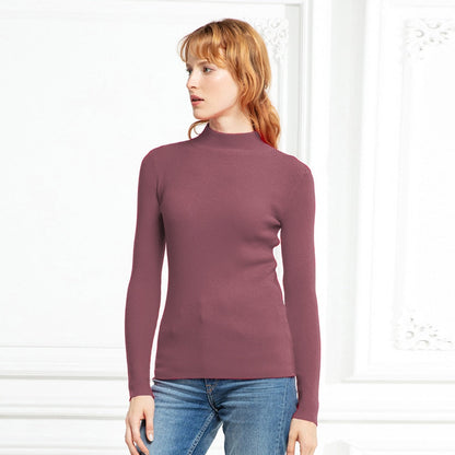 Frau in rosa Rollkragenpullover und blauer Jeans vor weißem Hintergrund.