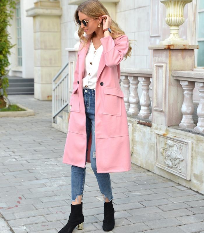 Frau in rosa Mantel, weiße Bluse, blaue Jeans, schwarze Stiefel, modisch, urbaner Hintergrund.