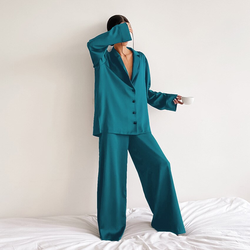 Frau in türkisfarbenem Satin-Pyjama mit Tasse, elegantes Nachtwäsche-Set, Schlafzimmer-Hintergrund.