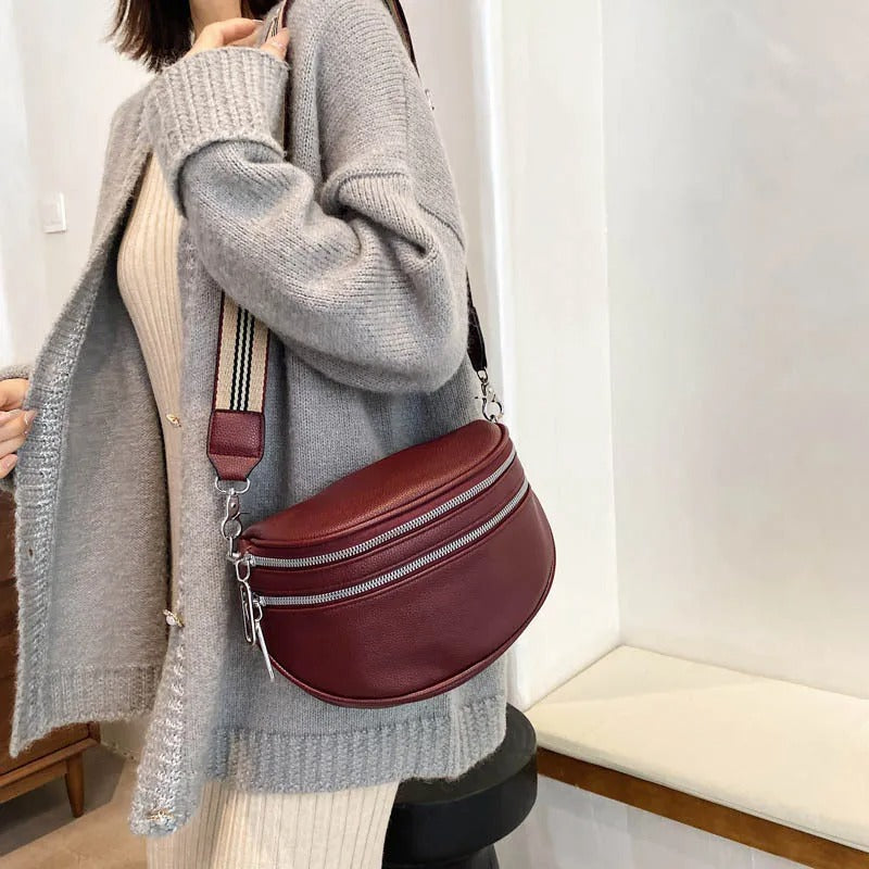 Frau mit grauem Strickcardigan und bordeauxroter Umhängetasche aus Leder im modernen Stil.