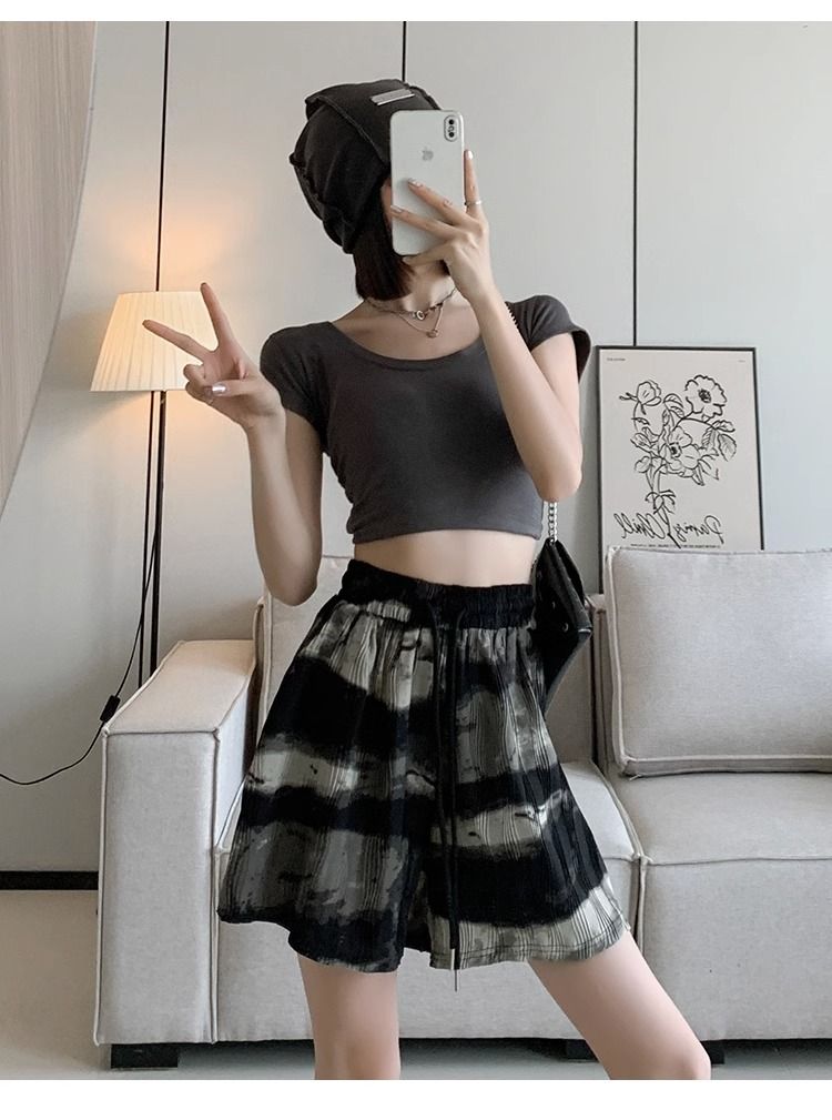 Frau in schwarzem Crop-Top und gestreiftem Rock macht Selfie im modernen Wohnzimmer.