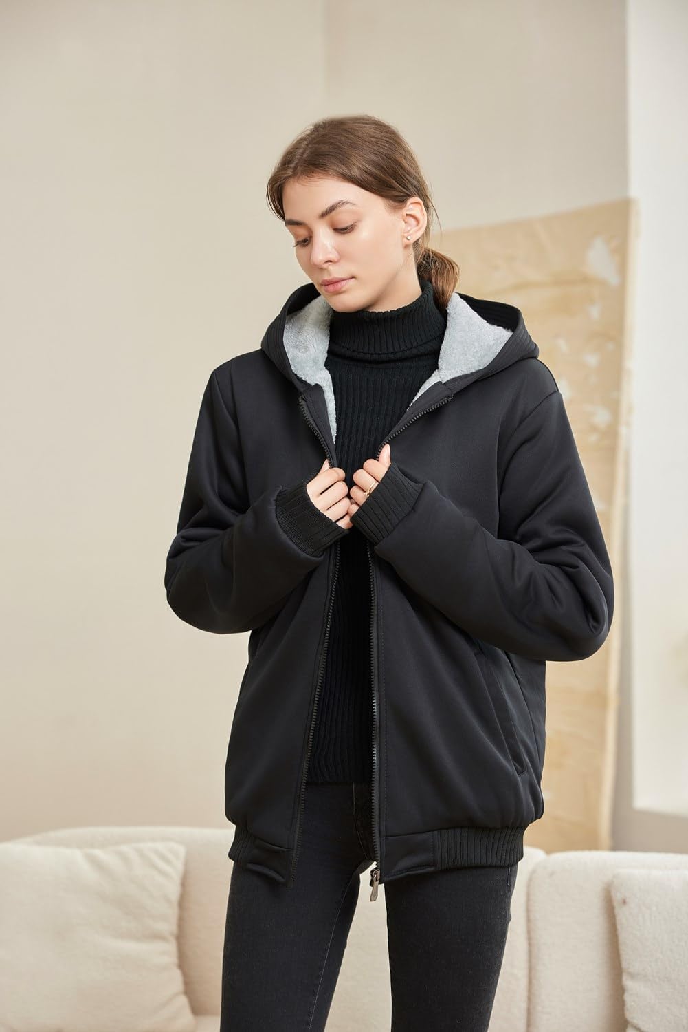Frau in schwarzer Kapuzenjacke, Reißverschluss, Innenfutter grau, modisch, bequem, warm.