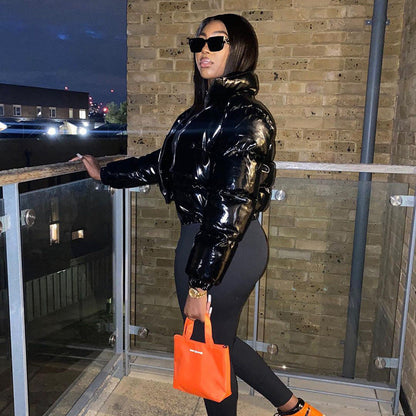Frau in schwarzer Lackjacke, Sonnenbrille, orange Tasche, steht auf Balkon bei Nacht.