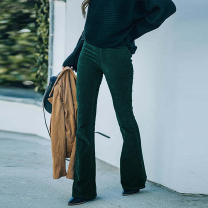 Frau in grüner Cordhose, schwarzem Pullover, hält braunen Mantel, modisch, Herbstkleidung.