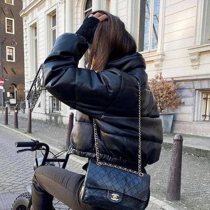 Frau in schwarzer Lederjacke auf Fahrrad, Chanel-Tasche, städtische Straße, Wintermode.