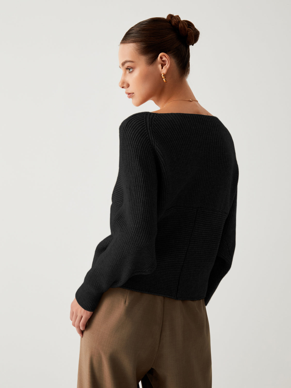 Frau in schwarzem Strickpullover und brauner Hose, eleganter Look, seitliches Profil.