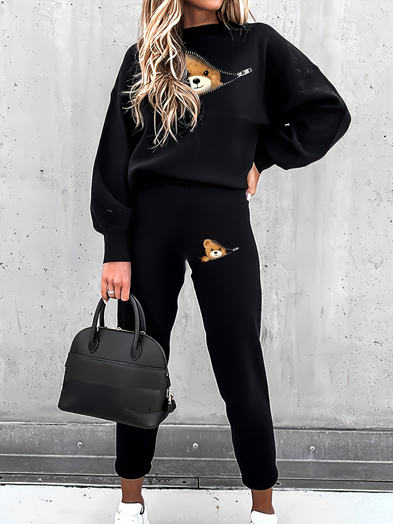 Frau in schwarzem Sweatshirt und Jogginghose mit Teddybär-Design, schwarze Handtasche.