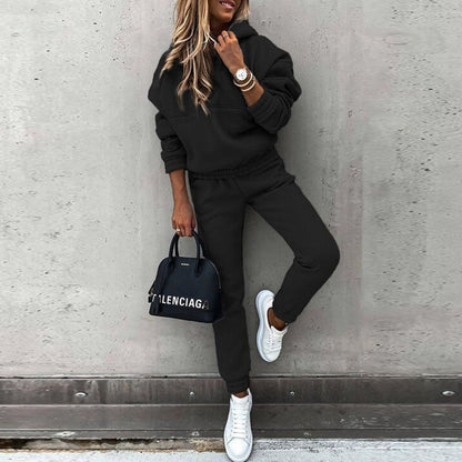 Frau in schwarzem Jogginganzug, weiße Sneaker, schwarze Handtasche, lässiger Streetstyle-Look.
