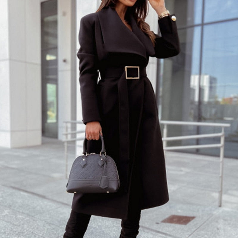 Frau in schwarzem Wollmantel mit Gürtel und schwarzer Handtasche vor modernem Gebäude.