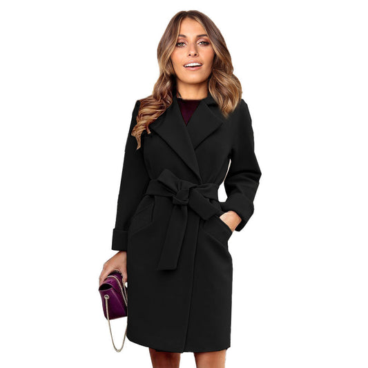 Frau in schwarzem Wollmantel mit Gürtel, hält lila Handtasche, elegante Herbstmode.