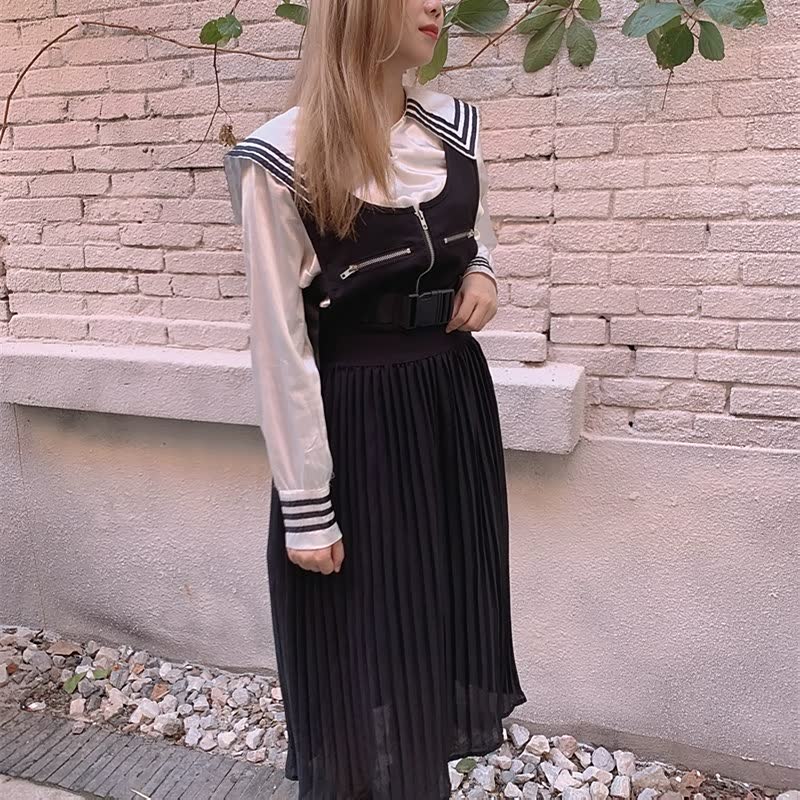 Frau in schwarz-weißem Schulmädchen-Outfit mit Faltenrock vor Ziegelwand.