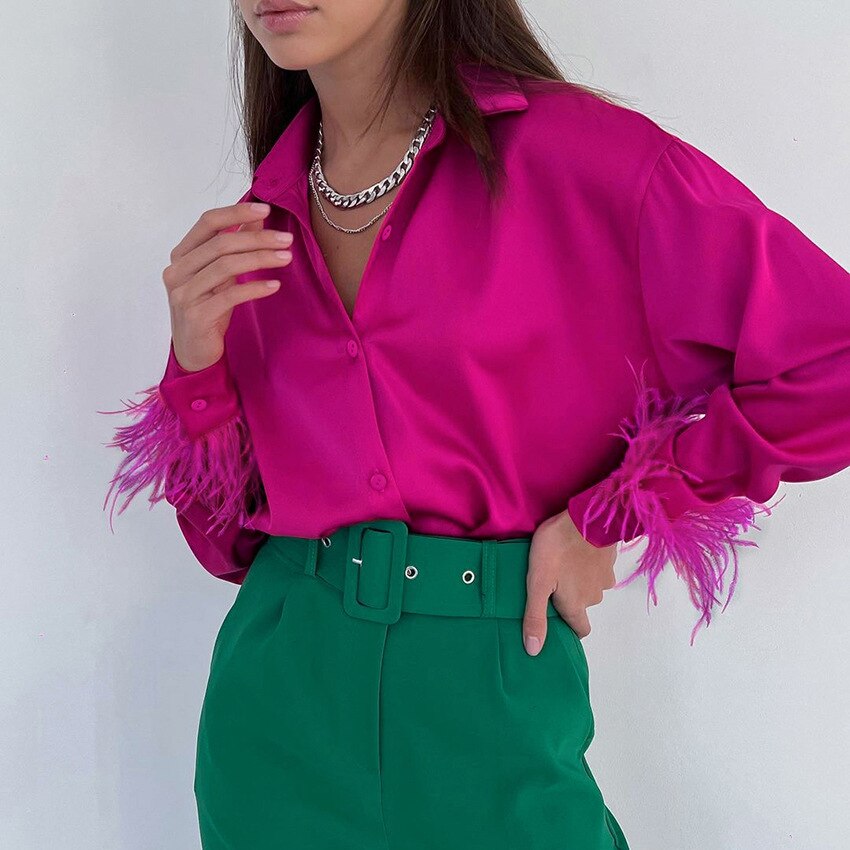 Frau in pinker Satinbluse mit Federn und grüner Hose, modisch, elegant, auffällige Farben.
