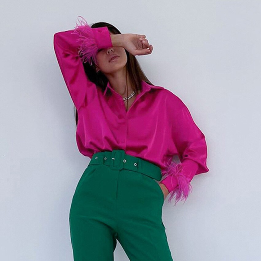 Frau in pinker Satinbluse mit Federn und grüner Hose, modisch, elegant, trendige Damenmode.