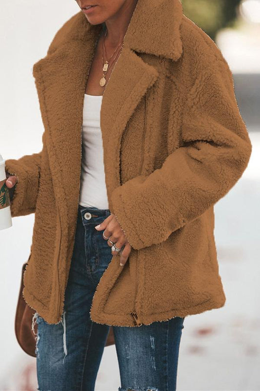 Frau in brauner Teddyjacke, weiße Bluse, Jeans, hält Kaffeebecher, Herbstmode.